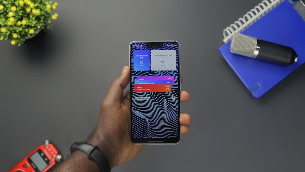 Close-up of a hand holding a smartphone displaying colorful notifications on a black surface.