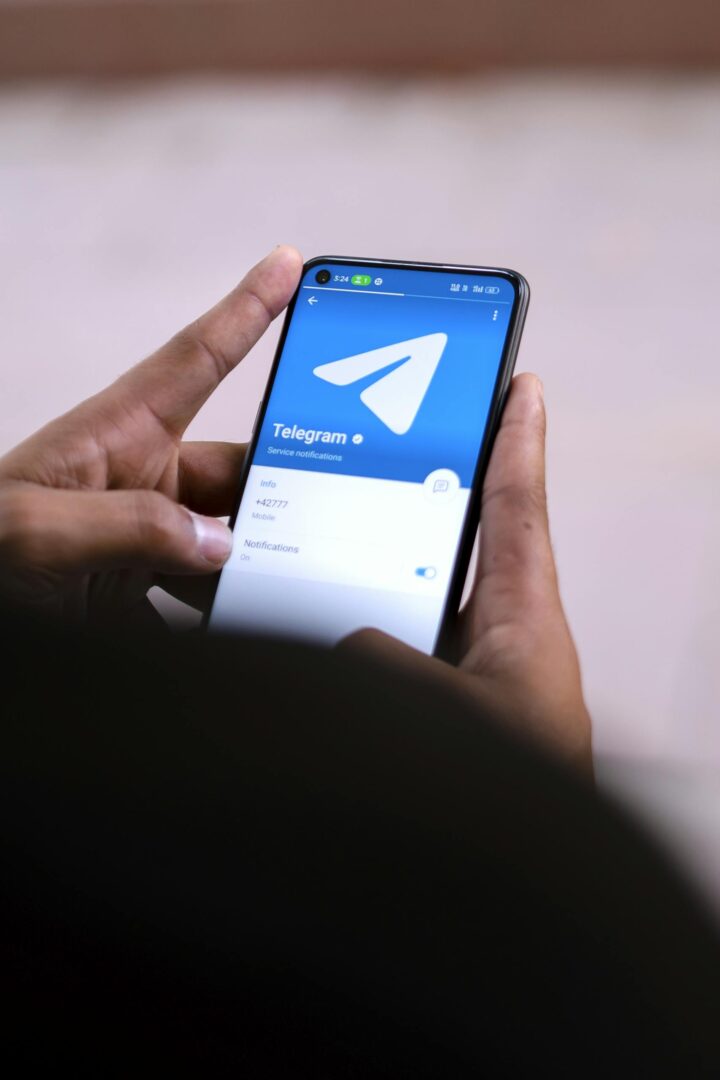 Close-up of hands holding a smartphone with the Telegram app open on the screen.